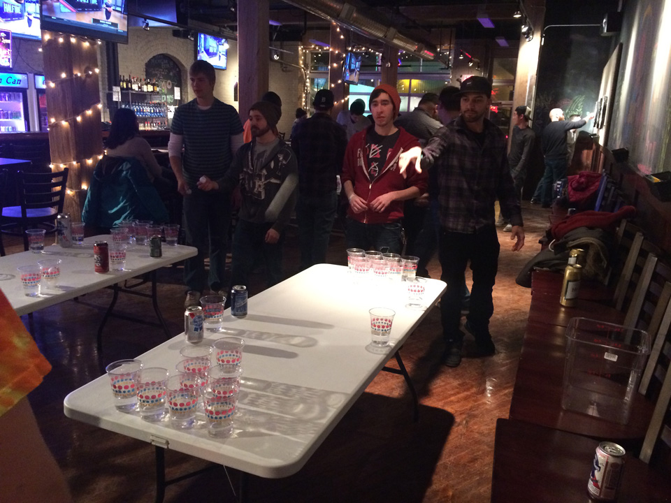 A beer pong game in full swing at Tin Can Bar with strings of lights overhead.