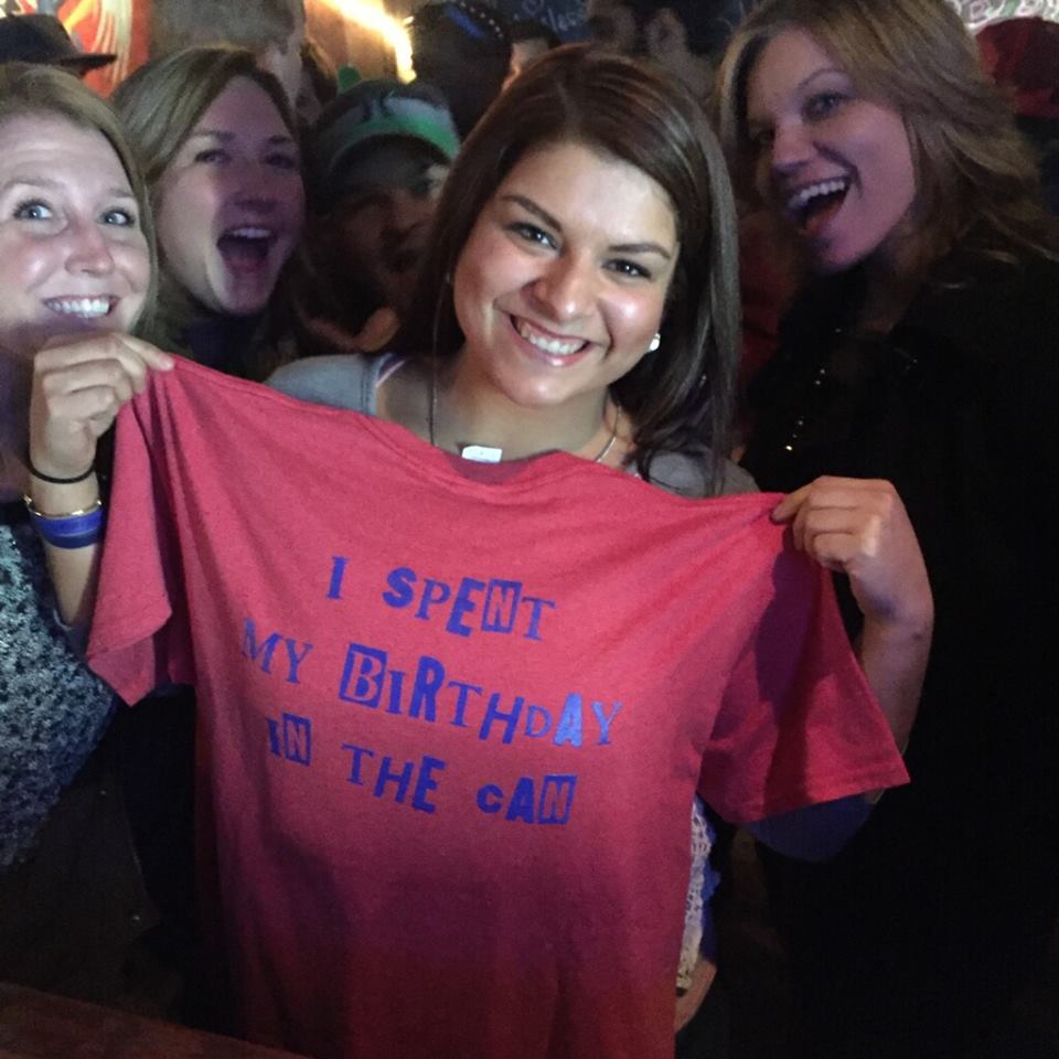 Woman holding an I Spent My Birthday in the Can t-shirt at Tin Can Bar.